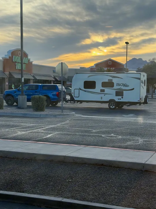 RV rental (Micro Lite travel trailer) towed by a blue pickup truck in a parking lot, with Dollar Tree & sunset sky.. Forest River Flagstaff Micro Lite XLT 2017