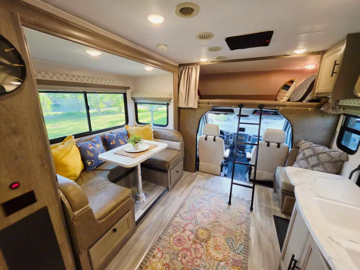 Bright rv rental interior: U-shaped dining area with windows, overhead bunk, kitchen counter, and front cabin for travel.. Forest River Coachmen Prism 2018