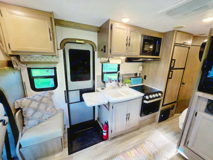 RV rental interior featuring a compact kitchen with a sink, stove, microwave, fridge, a cozy dinette, and exit door.. Forest River Coachmen Prism 2018