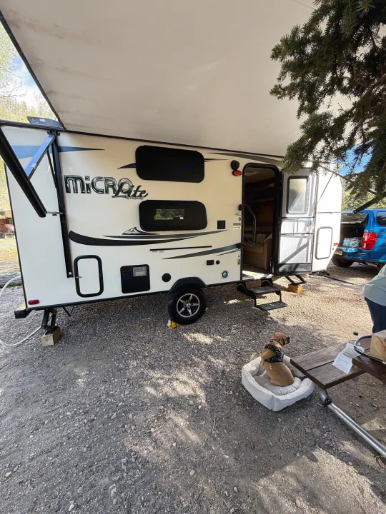 Micro Lite RV rental with awning extended at a gravel campsite. A dog rests by a picnic table, ready for adventure.. Forest River Flagstaff Micro Lite XLT 2017