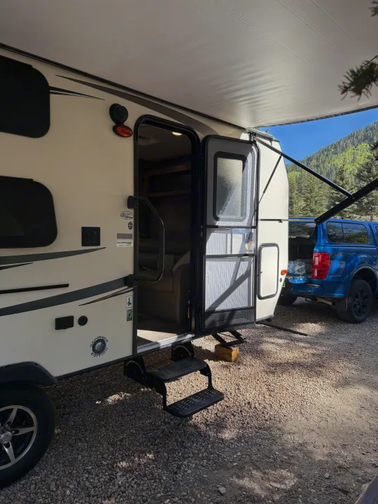 RV rental at a scenic campsite: awning extended, door open with steps, blue pickup truck parked behind.. Forest River Flagstaff Micro Lite XLT 2017