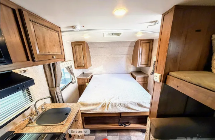 This RV rental interior features a cozy bedroom with overhead storage, a functional kitchen counter with a sink, and bunk beds.. Forest River Flagstaff Micro Lite XLT 2017