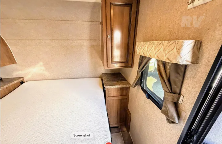 Inside an RV rental: a compact bedroom with a white mattress, wood cabinet, and window with beige curtains, offering cozy comfort.. Forest River Flagstaff Micro Lite XLT 2017