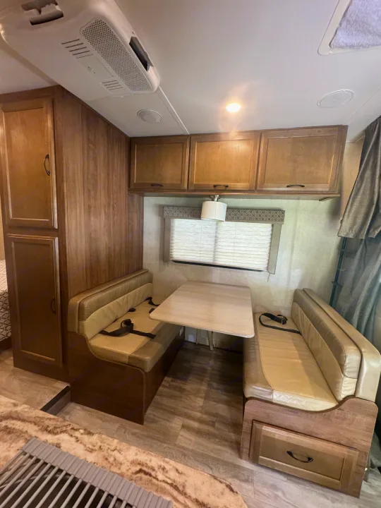 RV rental interior: dinette with tan booth seating, light wood table, overhead cabinets, and ceiling AC unit.. Gulf Stream Conquest 2019