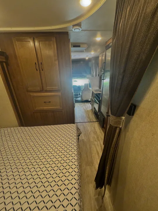 Spacious RV rental interior featuring a bedroom with patterned bedding, wood cabinets, a galley kitchen, and a view of the front cabin.. Gulf Stream Conquest 2019