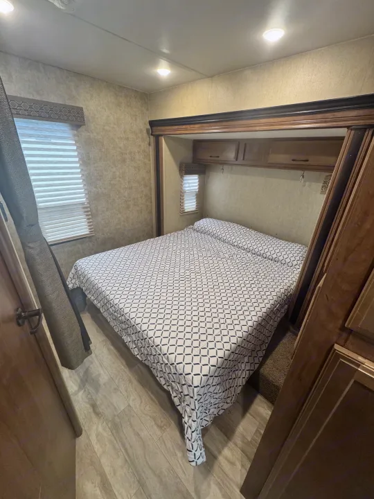 Comfortable RV rental bedroom showcasing a patterned bed, wood trim, blinds, and overhead cabinets.. Gulf Stream Conquest 2019