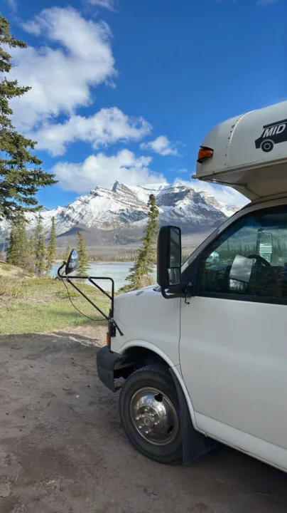A white camper van, likely an RV rental, is parked overlooking a turquoise river and majestic snow-capped mountains under a blue sky.. Chevrolet Express s3500 2003
