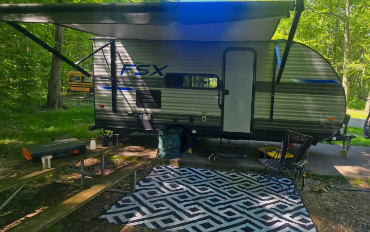 Salem FSX rv rental with awning extended at a shaded campsite, showing griddle and geometric rug.. Forest River Salem FSX 2020