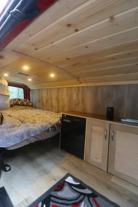 Cozy RV rental interior: wooden ceiling, comfy bed, kitchenette with mini-fridge & sink, plus wood flooring.. Glacier Campers Vanlife Explorer 2013