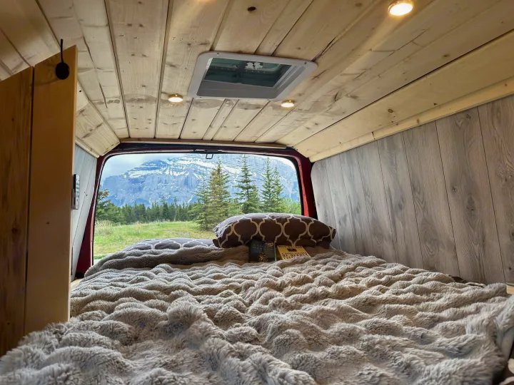 Relax in your rv rental's cozy bed with a fluffy blanket, offering picturesque mountain and forest views from the back.. Glacier Campers Vanlife Explorer 2013