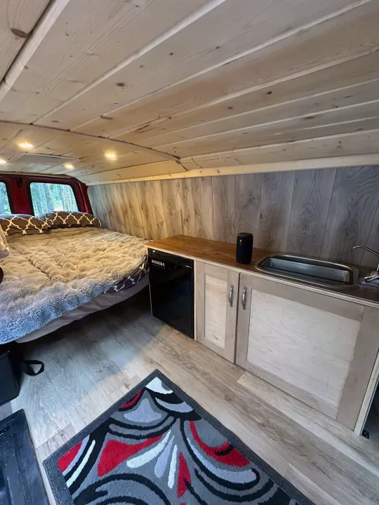 Cozy campervan interior with bed, kitchenette, wood finishes & colorful rug, perfect for an RV rental adventure.. Glacier Campers Vanlife Explorer 2013