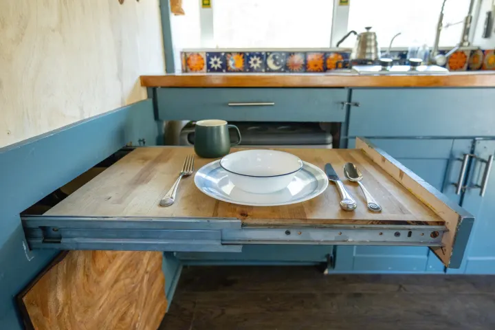 This RV rental features a practical pull-out dining table, set with dishes and cutlery, perfect for compact spaces.. Chevrolet Express s3500 2003