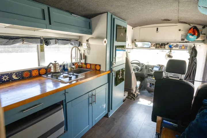 Rv rental interior: a converted vehicle's kitchen with blue cabinets, stove, sun/moon tiles, and view to the driver's cab.. Chevrolet Express s3500 2003