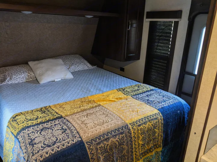 Cozy RV rental bedroom featuring a bed with a patterned throw, overhead storage, and a window for comfortable travel accommodation.. Jayco Jay Flight 2020