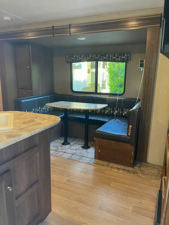 Experience comfort in this RV rental's dinette area, featuring black booth seating, a table, a window, and wood-look floors.. Dutchmen Coleman Lantern 2018
