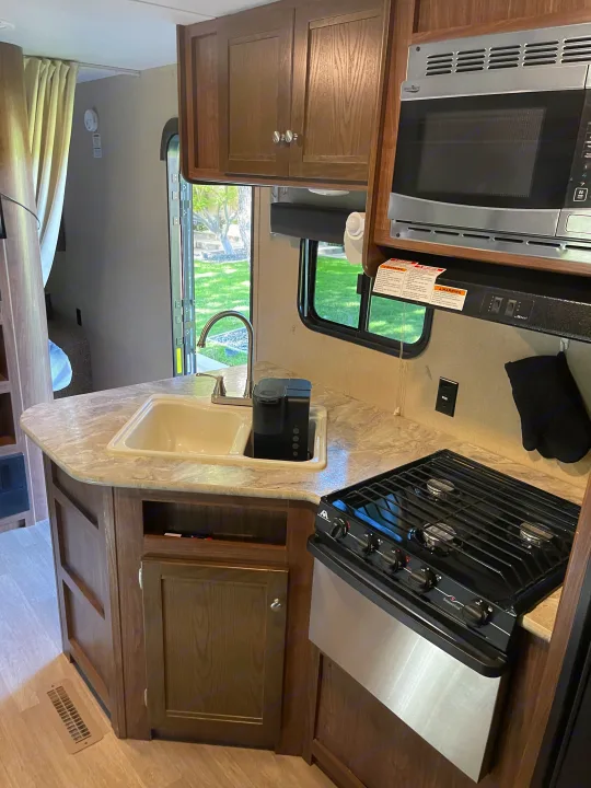 RV rental kitchen: Features a sink, microwave, stove, coffee maker, and wood cabinetry, providing a functional space.. Dutchmen Coleman Lantern 2018