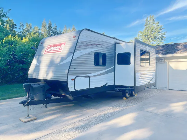 This grey Coleman RV rental travel trailer with its slide-out extended is parked on a sunny driveway, ready for new adventures.. Dutchmen Coleman Lantern 2018