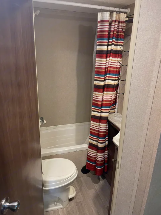 Compact RV rental bathroom featuring a shower/tub, toilet, and vanity with a striped curtain, ideal for travel.. Dutchmen Coleman Lantern 2018