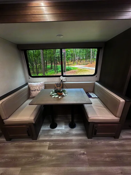 Inviting RV rental dinette with cozy booth seating, a central table, and a large window offering forest views.. Grand Design Transcend Xplor 2024