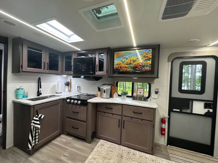 Modern RV rental kitchen with gray cabinets, marble counters, full appliances, a TV, and skylights.. Grand Design Transcend Xplor 2024