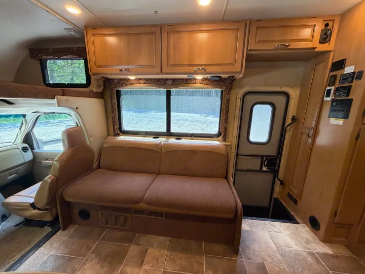 Inside this RV rental: a cozy living area with a sofa, large windows, storage cabinets, and an entry door.. Thor Four Winds 2016