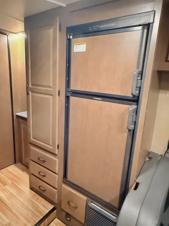 RV rental interior showing a Dometic refrigerator with wood paneling, alongside cabinets and light wood flooring.. Thor Majestic 2020