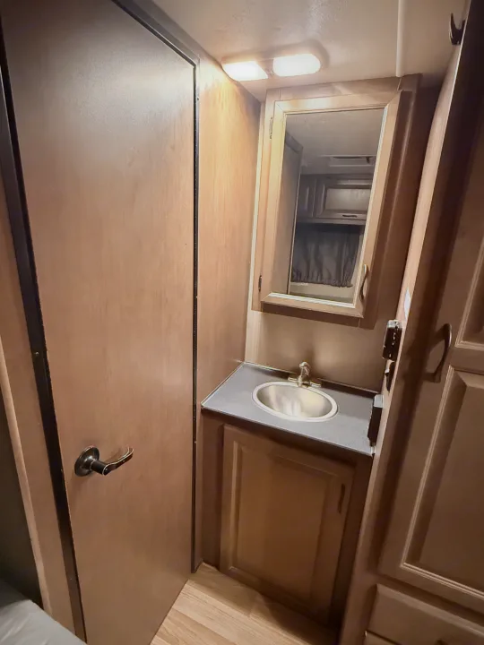 This RV rental bathroom offers a compact vanity with sink, mirrored cabinet, and warm wood finishes, providing travel convenience.. Thor Majestic 2020