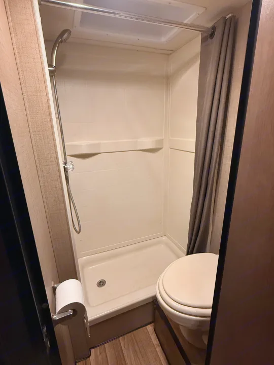 Compact RV rental bathroom featuring a shower with a handheld showerhead, toilet, and shower curtain.. Thor Majestic 2020