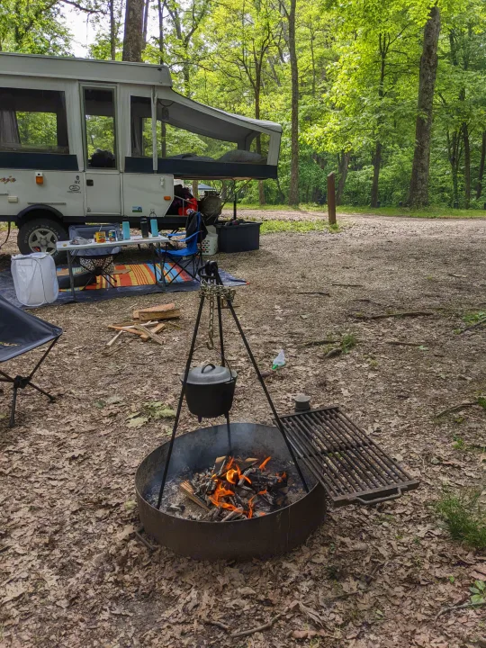 Cozy rv rental camper setup at a forest campsite with a crackling campfire, Dutch oven cooking, and a table for outdoor meals.. Jayco Qwest 2004