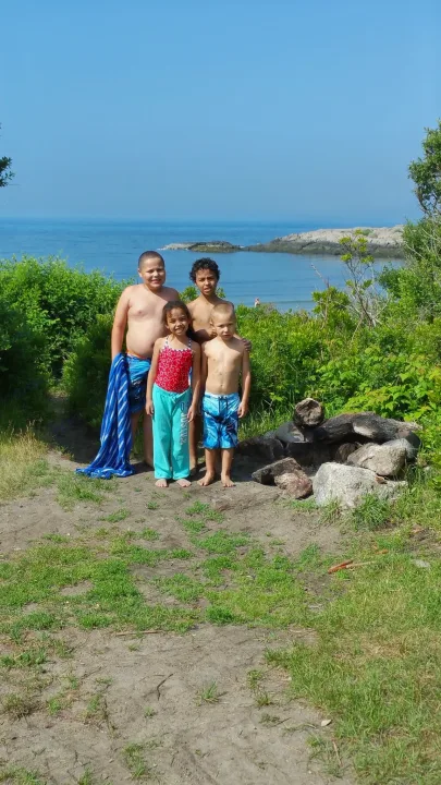 Four happy kids by the ocean, surrounded by green foliage. An RV rental is perfect for family trips to scenic coastal spots like this.. Jayco Qwest 2004