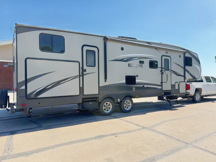 This large grey REZERVE Crossroads fifth-wheel RV, suitable for RV rental, is hitched to a white pickup truck.. Crossroads RV Rezerve 2015