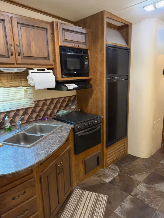 Compact RV kitchen with sink, microwave, stove, fridge, and ample storage, ideal for an rv rental.. Crossroads RV Rezerve 2015