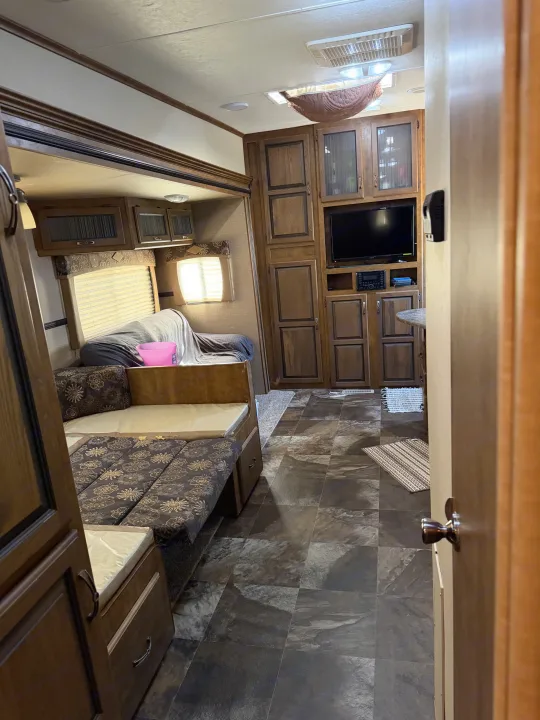 RV rental interior: living area with wood cabinets, mounted TV, comfy bench seating, and dark tiled floor.. Crossroads RV Rezerve 2015