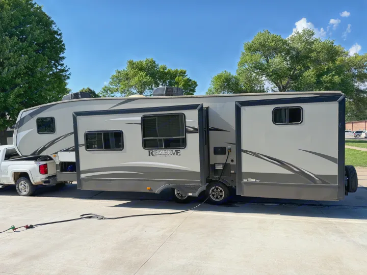 This spacious gray fifth-wheel RV rental, with extended slide-outs, is hitched to a pickup and powered up, ready for travel.. Crossroads RV Rezerve 2015