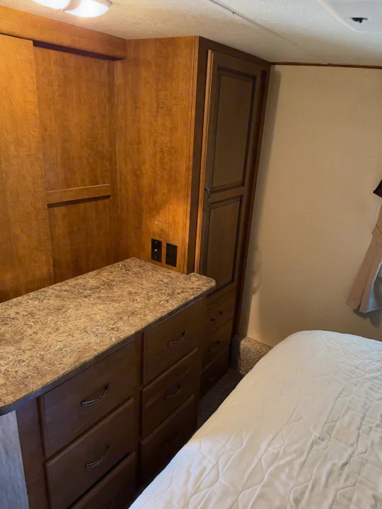 Cozy RV rental bedroom featuring wood-toned cabinetry, a dresser with countertop, and a comfortable bed for restful travel.. Crossroads RV Rezerve 2015