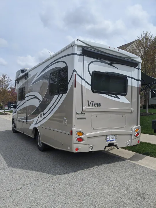 Winnebago View rv rental: a cream and gray motorhome with an Indiana plate, parked on a street under a cloudy sky.. Winnebago View 24G 2016