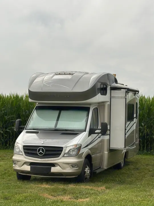 Winnebago RV rental, a Mercedes-Benz Class C motorhome with a slide-out, parked in a cornfield under an overcast sky.. Winnebago View 24G 2016