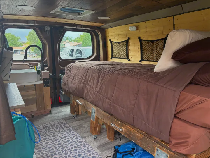 Cozy RV rental interior with a comfy bed, kitchenette, and wood paneling. Perfect for van life adventures!. FORD TRANSIT 250 2015