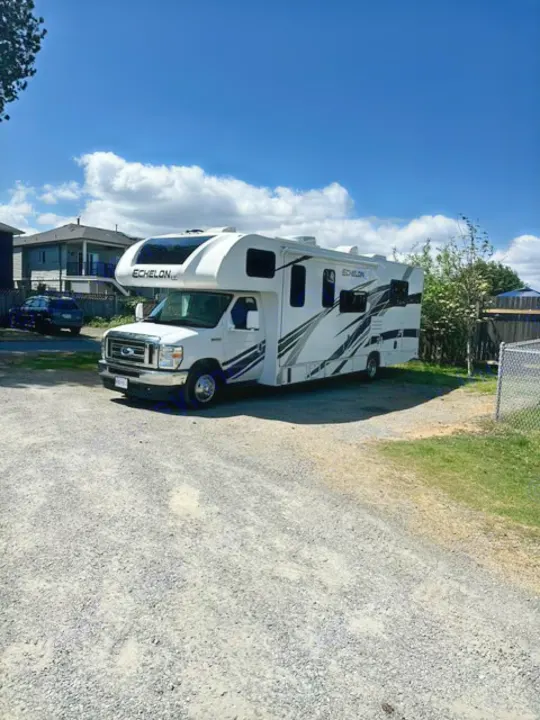 White Echelon RV rental parked on a sunny gravel lot under a blue sky, ready for your travel and camping trip.. Thor Echelon 2022
