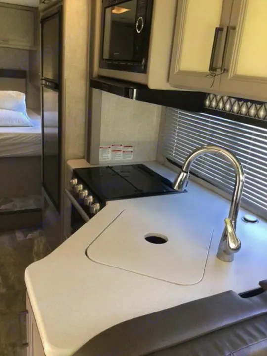 This RV rental interior features a compact kitchen with a stove, microwave, sink, and a view of the adjacent sleeping area.. Thor Echelon 2022