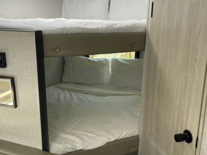 Cozy bunk beds with white bedding inside a modern RV rental, offering comfortable sleeping arrangements for travelers.. East to West Silver Lake 2023