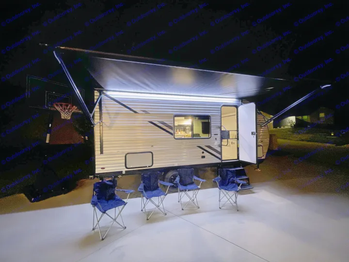 Enjoy your rv rental! Brightly lit travel trailer at night with extended awning and four camping chairs. Perfect for outdoor relaxing.. East to West Silver Lake 2023