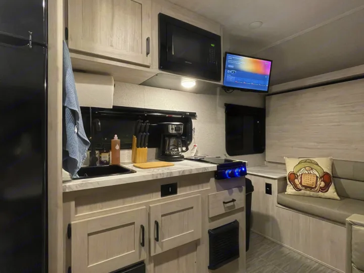 Inside this RV rental, find a modern kitchen with microwave, coffee maker, and stovetop, plus a cozy dining nook and TV.. East to West Silver Lake 2023