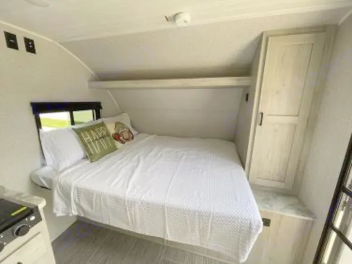 Comfortable RV rental bedroom featuring a large bed with white bedding, window, overhead shelf, and wardrobe cabinet.. East to West Silver Lake 2023