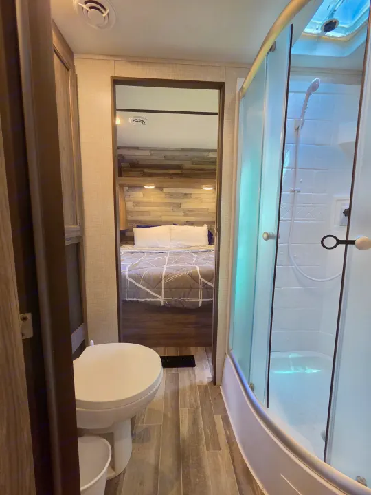 This RV rental features a compact bathroom with a toilet and shower, looking through to a bedroom with a cozy bed.. Crossroads RV Zinger 2021
