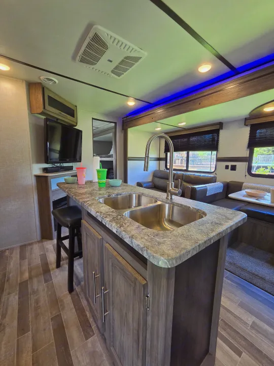 RV rental's modern interior: kitchen island with double sink, TV, seating, and bunk beds. Features accent lighting.. Crossroads RV Zinger 2021