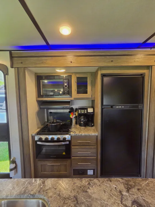 RV rental kitchen: microwave, stove, oven, fridge, coffee maker, and blue accent lighting. Practical space for on-the-go meals.. Crossroads RV Zinger 2021