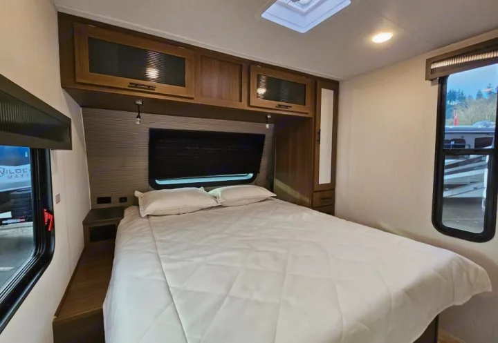 Cozy RV rental bedroom with white bed, overhead cabinets, and large window. Features storage & bright interior.. Forest River 246DBX 2026