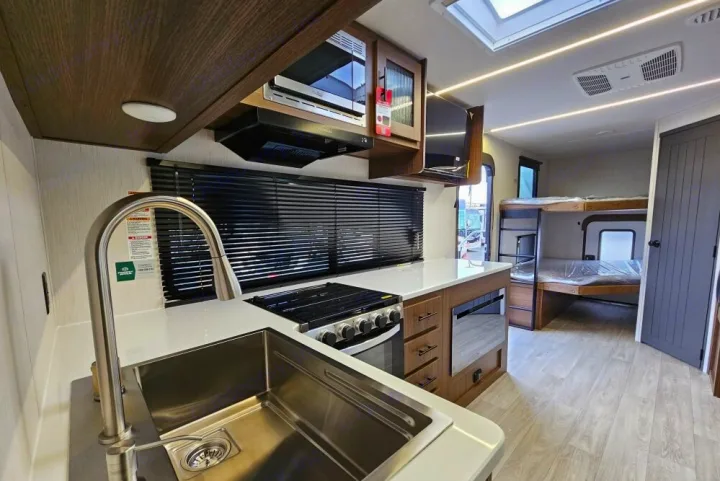 Modern RV rental interior: kitchen with sink, stove, microwave, cabinets, and bunk beds. Bright, clean, and ready for adventure.. Forest River 246DBX 2026
