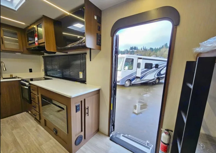 Modern RV rental kitchen with sleek appliances and an open door showing another RV outside.. Forest River 246DBX 2026